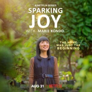 Sparking Joy with Marie Kondo. Marie Kondo ist vor Bäumen und Sträuchern abgebildet. Sie lächelt.