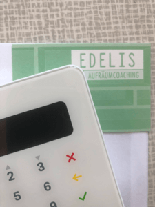 Das Bild zeigt einen gemuterten Hintergrund, eine Visitenkarte von "Edelis Aufräumcoaching" und einen Teil eines Kartenterminals.